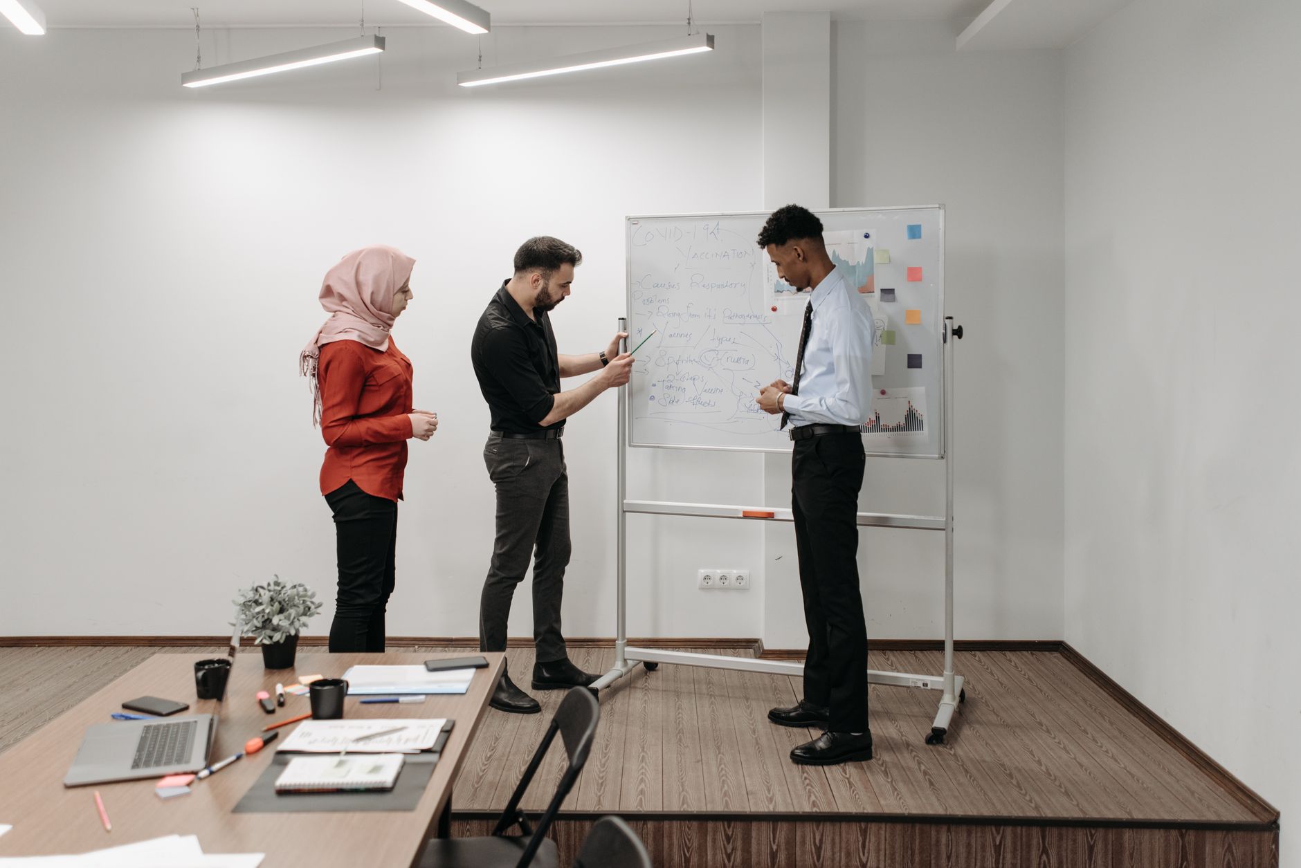 Three professionals discussing project ideas during an office meeting, illustrating teamwork and diversity.